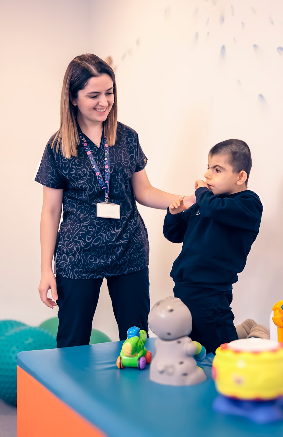 Eine Frau führt die Hand eines kleinen Jungen in einem Therapieraum.